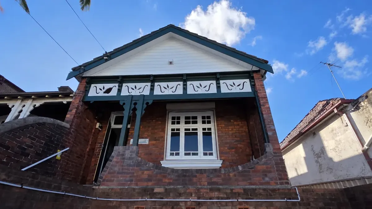 Federation brick home in Sydney with deep green trims and a white fretwork gable under a clear summer sky