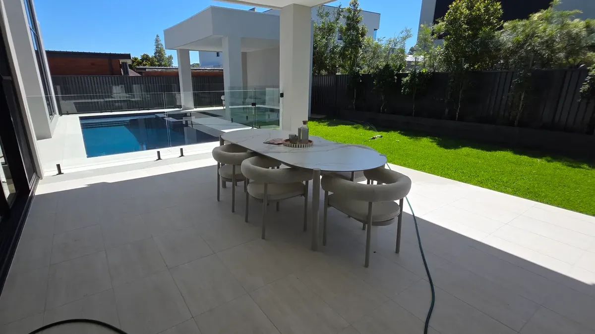 Outdoor dining area beside a pool in Sydney with white rendered walls and a dark painted fence